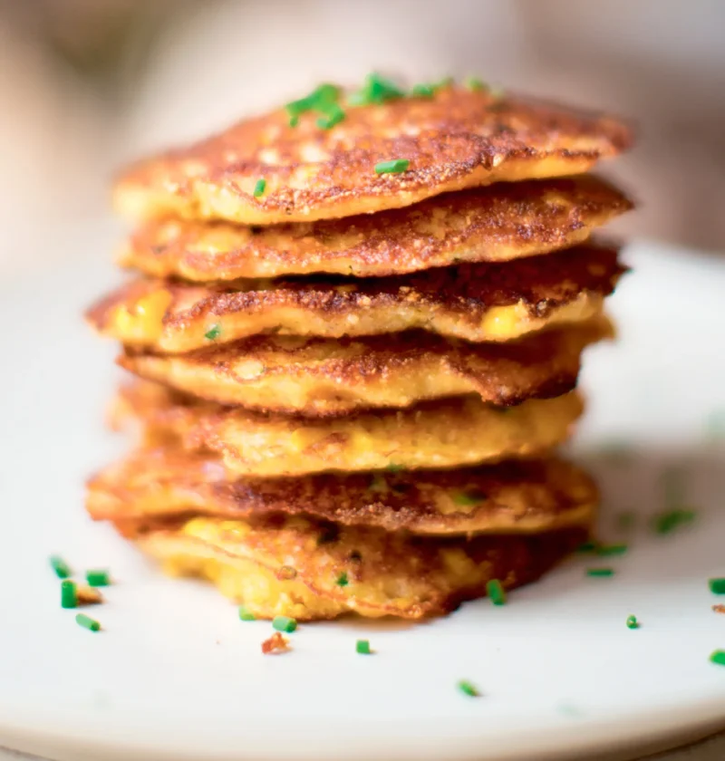 Stack of golden Ina Garten fresh corn pancakes topped with minced chives on a white plate