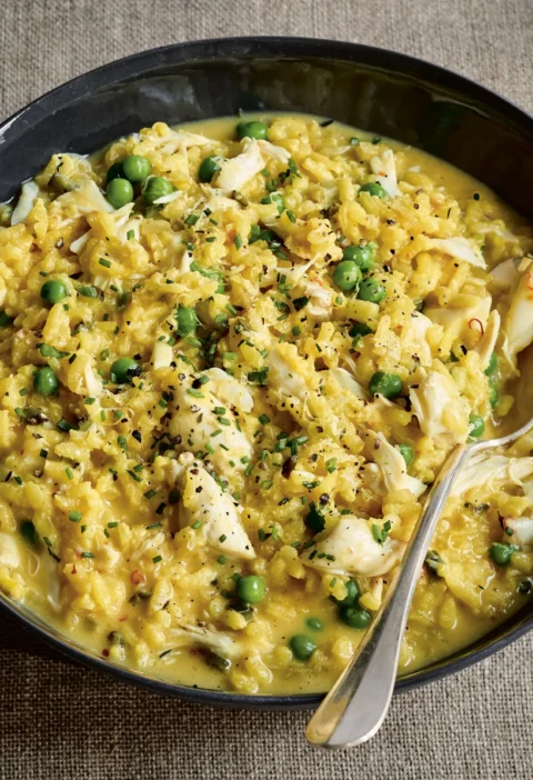 Ina Garten fresh crab & pea risotto with lump crabmeat, green peas, chives and lemon zest in a dark shallow bowl with a spoon