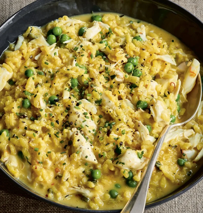 Ina Garten fresh crab & pea risotto with lump crabmeat, green peas, chives and lemon zest in a dark shallow bowl with a spoon