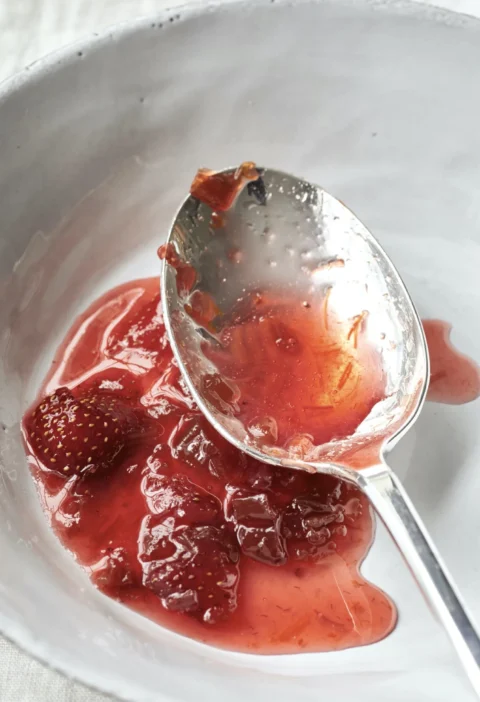 Ina Garten fresh strawberry rhubarb preserves in a white bowl with a silver spoon lifting a spoonful of jammy fruit