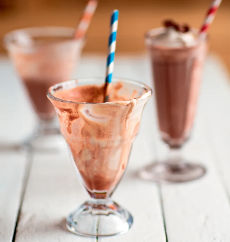 Ina Garten frozen hot chocolate in ice cream soda glasses with striped paper straws on a white wooden table