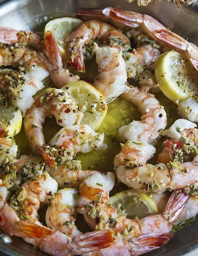 Ina Garten garlic and herb roasted shrimp in a pan with lemon slices, rosemary and garlic butter