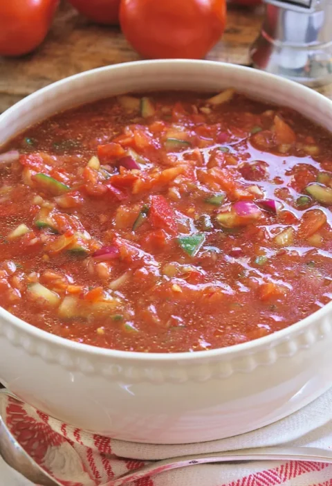 Ina Garten gazpacho in a white bowl with chunky tomatoes, cucumbers and red onions