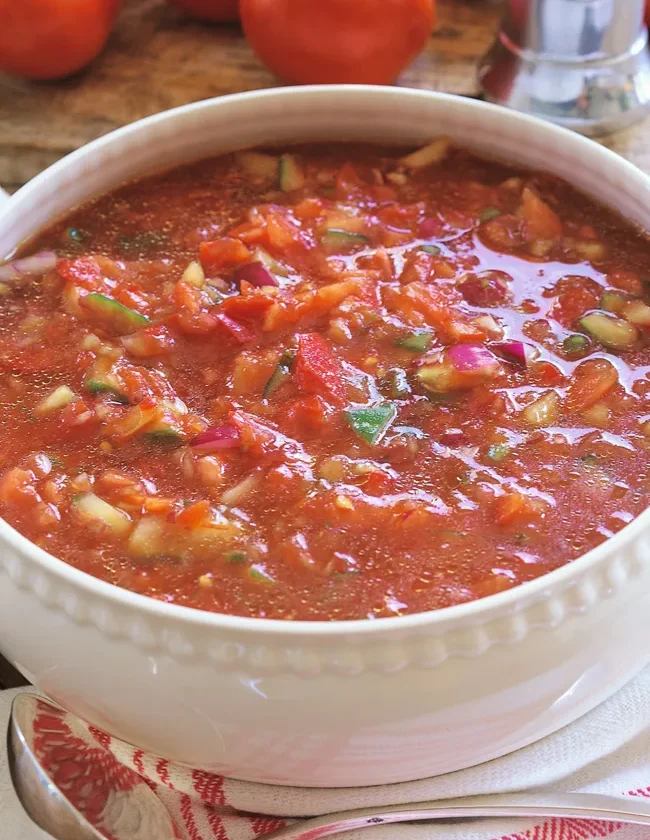 Ina Garten gazpacho in a white bowl with chunky tomatoes, cucumbers and red onions