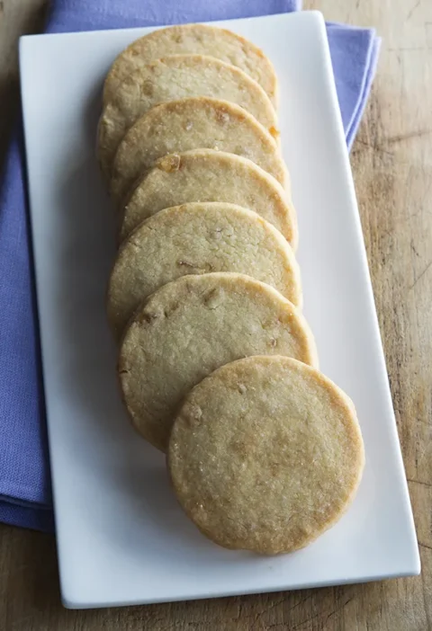 Ina Garten ginger shortbread cookies lined up on a white rectangular plate over a purple napkin