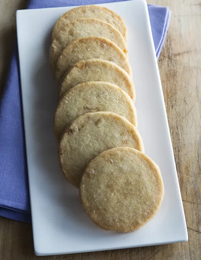 Ina Garten ginger shortbread cookies lined up on a white rectangular plate over a purple napkin