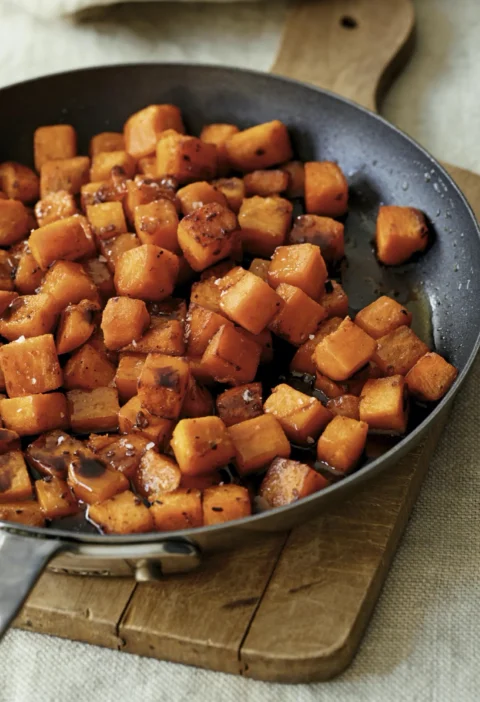 Ina Garten glazed sweet potatoes, diced and caramelized in a skillet on a wooden board