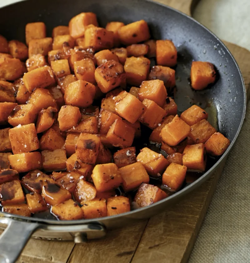 Ina Garten glazed sweet potatoes, diced and caramelized in a skillet on a wooden board