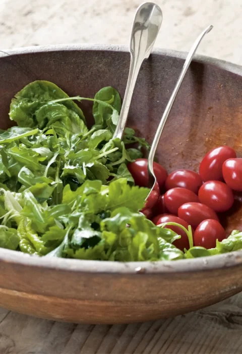 Ina Garten green salad vinaigrette tossed with fresh arugula in a rustic wooden bowl with grape tomatoes