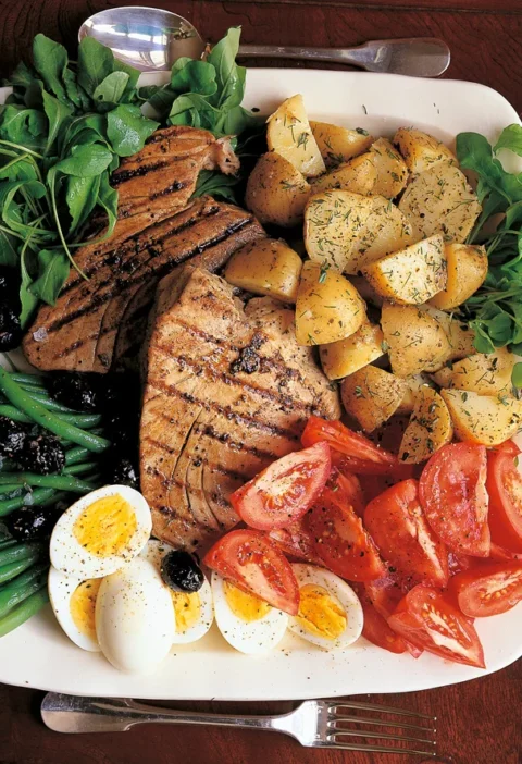 Ina Garten grilled tuna niçoise platter with seared tuna steaks, potato salad, tomato wedges, halved eggs, haricots verts and olives on a white platter
