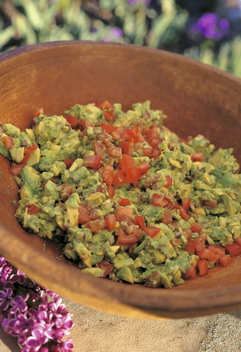 Ina Garten guacamole, chunky mashed avocado topped with diced tomato in a wooden bowl