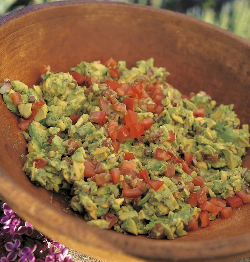Ina Garten guacamole, chunky mashed avocado topped with diced tomato in a wooden bowl