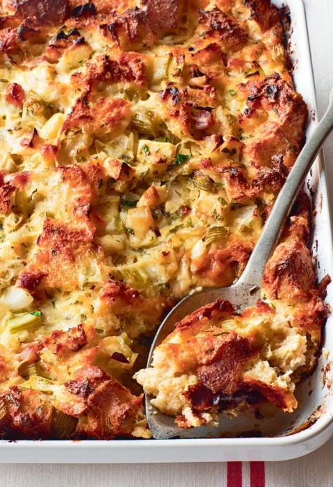 Ina Garten herb and apple bread pudding baked golden brown in a white baking dish with a serving spoon