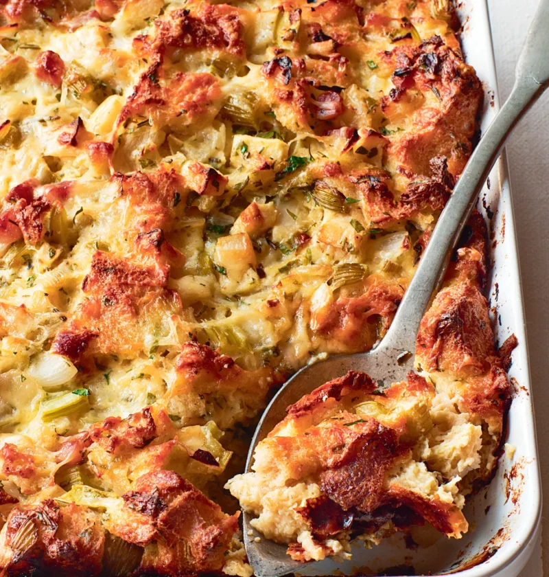 Ina Garten herb and apple bread pudding baked golden brown in a white baking dish with a serving spoon