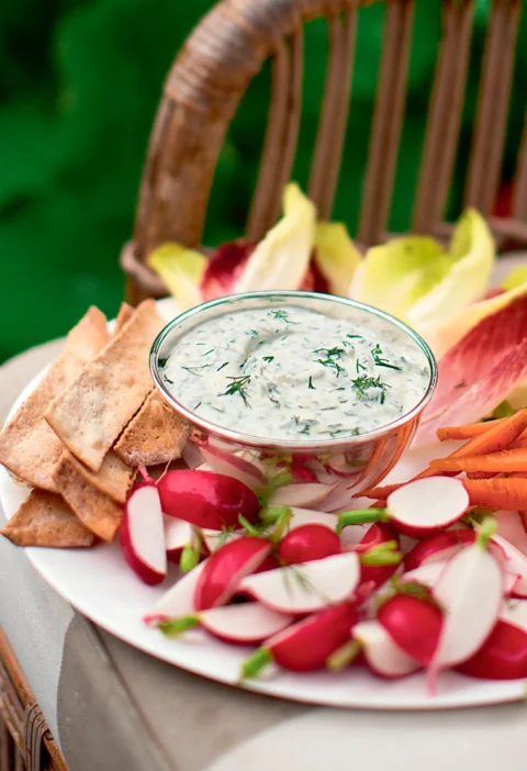 Ina Garten herbed fromage blanc dip with fresh dill in a glass bowl surrounded by radishes, carrots and crackers