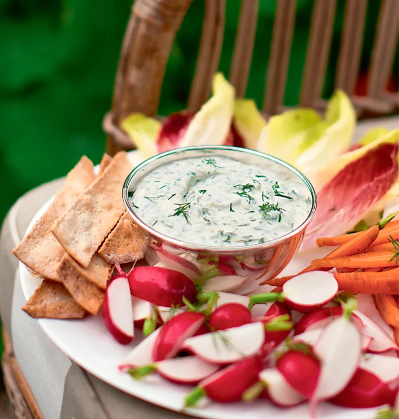 Ina Garten herbed fromage blanc dip with fresh dill in a glass bowl surrounded by radishes, carrots and crackers