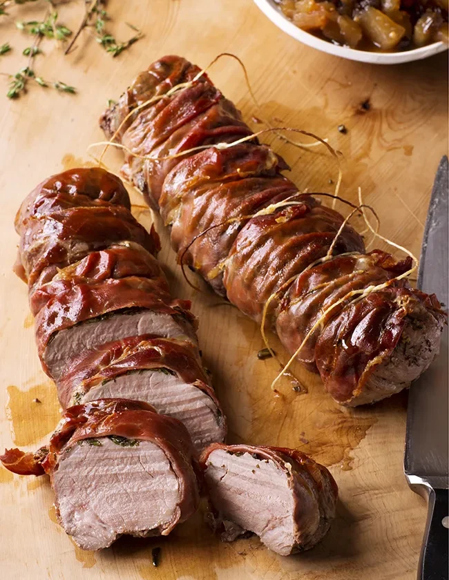 Ina Garten herbed pork tenderloins with apple chutney, prosciutto-wrapped and sliced on a wooden cutting board