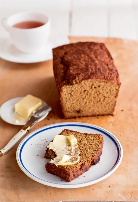 Ina Garten Irish Guinness brown bread loaf with one buttered slice on a blue-rimmed plate and a cup of tea