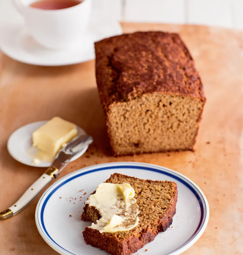 Ina Garten Irish Guinness brown bread loaf with one buttered slice on a blue-rimmed plate and a cup of tea