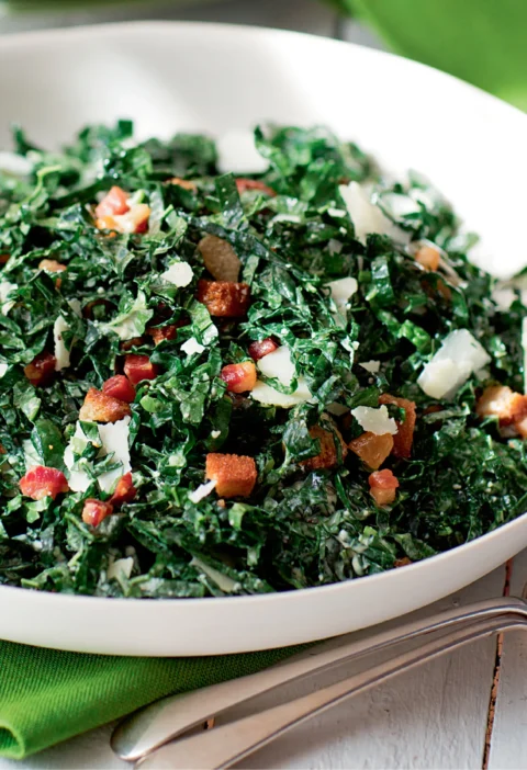 Ina Garten kale salad with pancetta and pecorino in a white bowl with crispy pancetta, bread cubes and shaved cheese