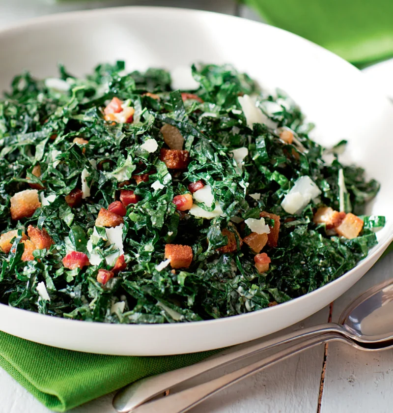 Ina Garten kale salad with pancetta and pecorino in a white bowl with crispy pancetta, bread cubes and shaved cheese