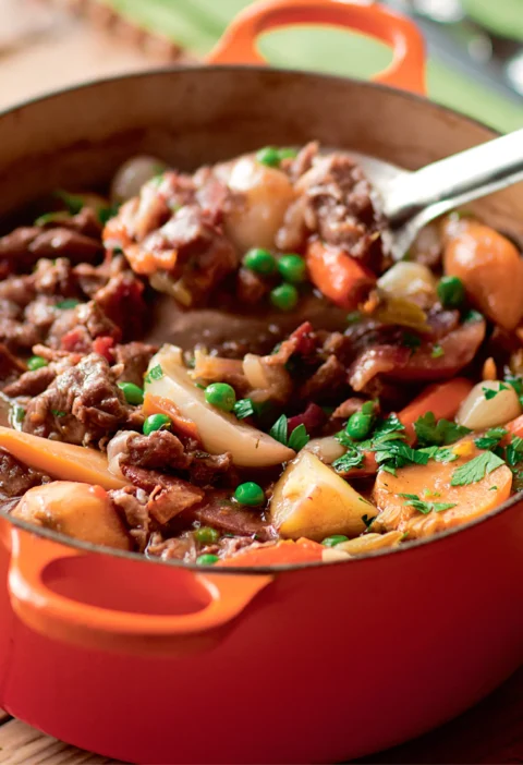 Ina Garten lamb stew with spring vegetables in an orange Dutch oven with carrots, potatoes, peas and parsley