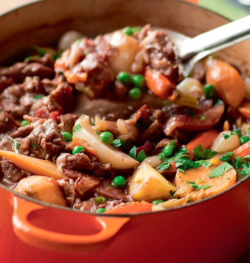 Ina Garten lamb stew with spring vegetables in an orange Dutch oven with carrots, potatoes, peas and parsley