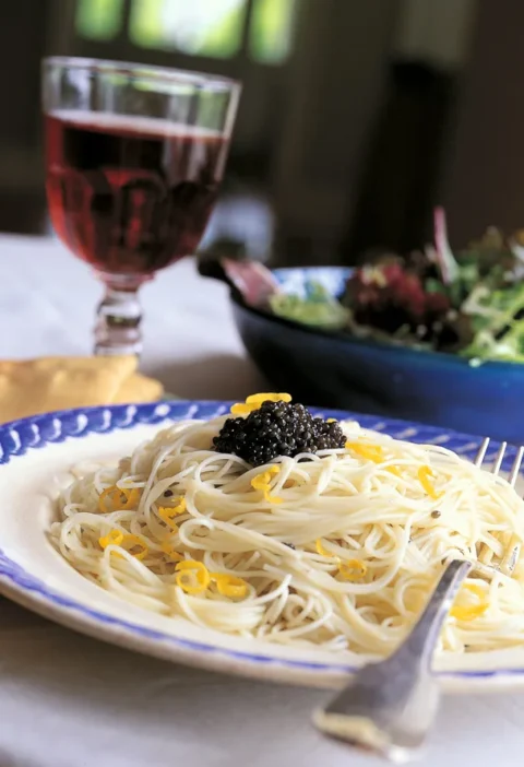 Ina Garten lemon capellini with caviar on a blue-rimmed plate topped with black caviar and lemon zest