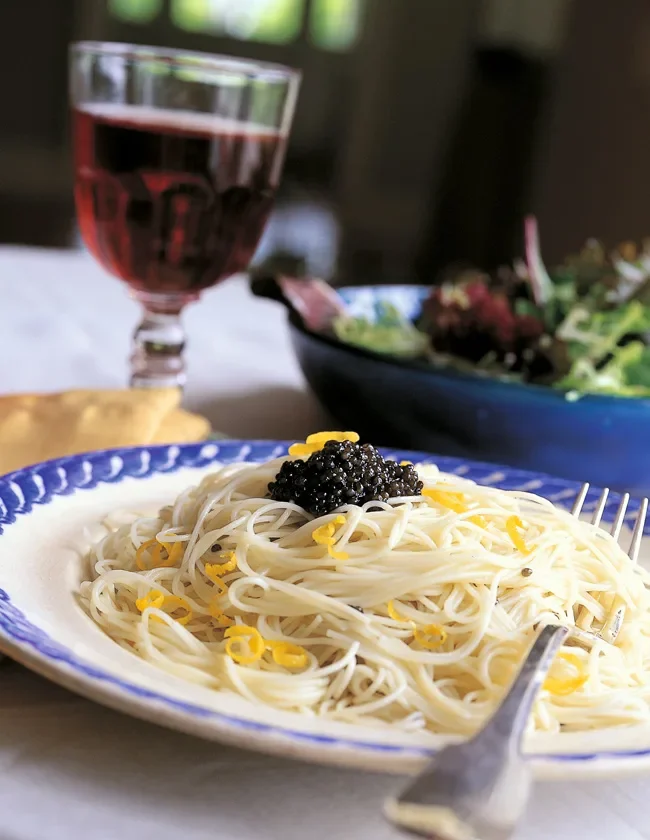 Ina Garten lemon capellini with caviar on a blue-rimmed plate topped with black caviar and lemon zest