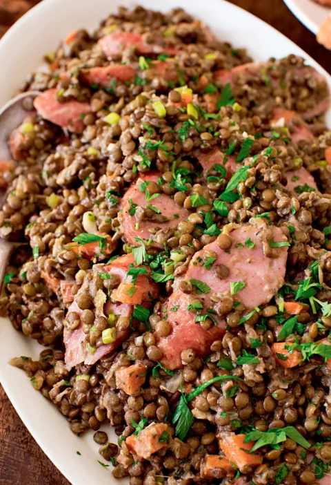 Ina Garten lentil and kielbasa salad with sliced kielbasa, diced carrots and parsley on an oval white platter