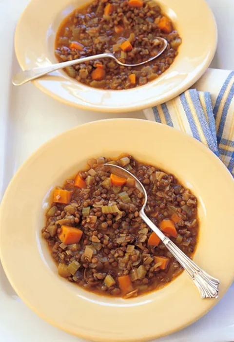 Two plates of Ina Garten lentil vegetable soup with green lentils, carrots and celery and silver spoons