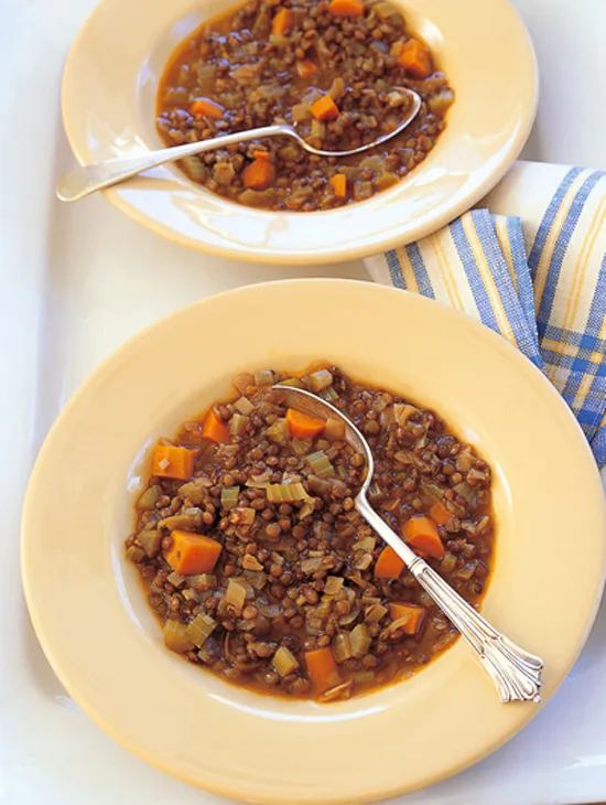 Two plates of Ina Garten lentil vegetable soup with green lentils, carrots and celery and silver spoons