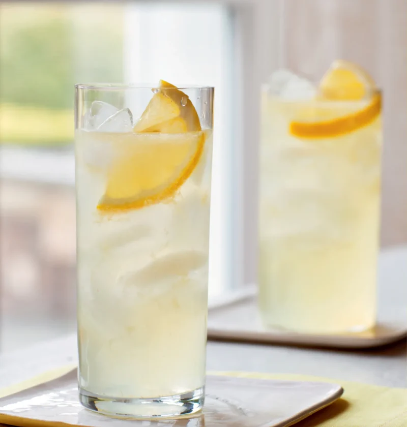 Two tall glasses of Ina Garten limoncello vodka collins with ice and lemon slices on a yellow napkin