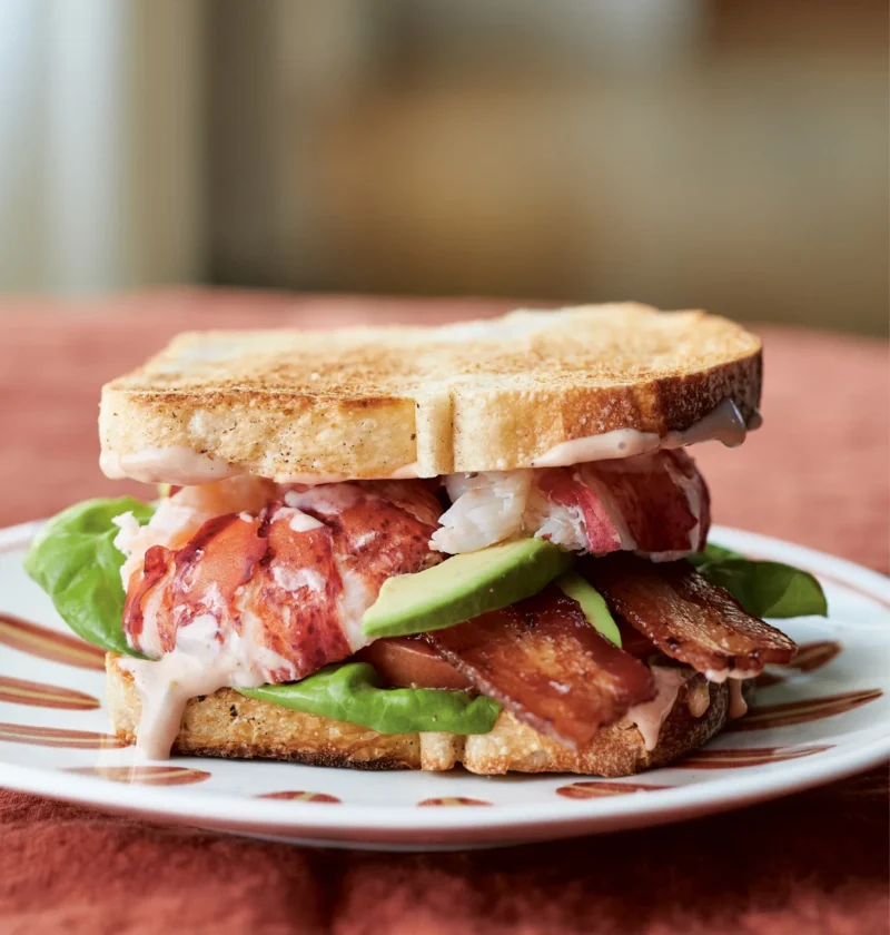 Ina Garten lobster BLTs with lobster meat, bacon, avocado, tomato and lettuce between toasted white bread on a plate