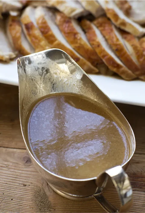 Silver gravy boat filled with Ina Garten make-ahead turkey gravy with onions and sage next to sliced roast turkey