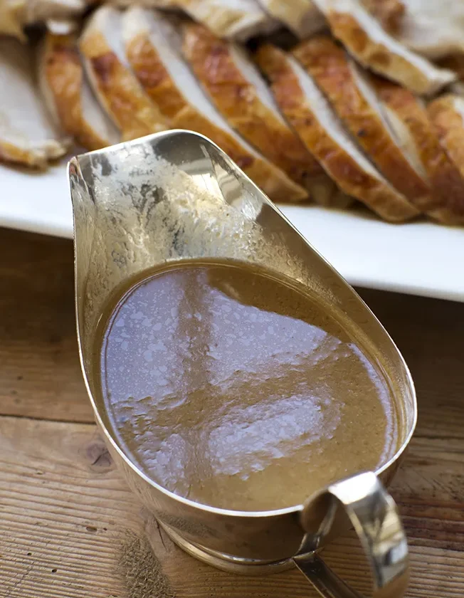 Silver gravy boat filled with Ina Garten make-ahead turkey gravy with onions and sage next to sliced roast turkey