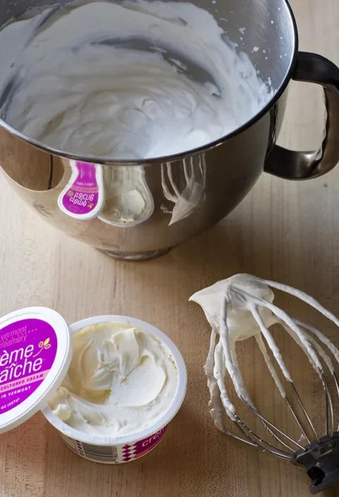 Ina Garten make-ahead whipped cream in a stand mixer bowl next to a whisk and a tub of crème fraîche