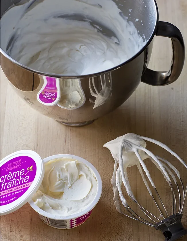 Ina Garten make-ahead whipped cream in a stand mixer bowl next to a whisk and a tub of crème fraîche