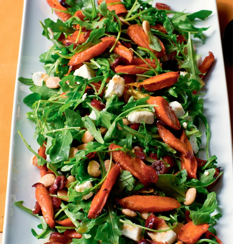 Ina Garten maple-roasted carrot salad with arugula, goat cheese, dried cranberries and Marcona almonds on a white platter