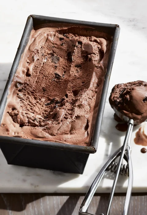 Ina Garten milk chocolate Oreo ice cream in a metal loaf pan with an ice cream scoop of chocolate ice cream with cookie pieces beside it