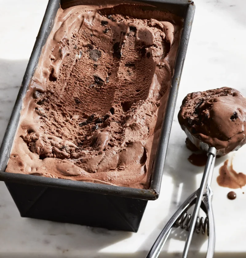Ina Garten milk chocolate Oreo ice cream in a metal loaf pan with an ice cream scoop of chocolate ice cream with cookie pieces beside it