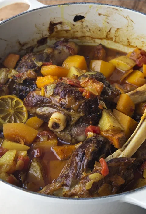 Ina Garten Moroccan lamb tagine with lamb shanks, butternut squash, tomatoes and a roasted lime slice in a white Dutch oven