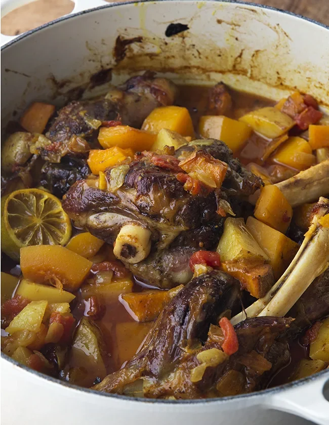 Ina Garten Moroccan lamb tagine with lamb shanks, butternut squash, tomatoes and a roasted lime slice in a white Dutch oven