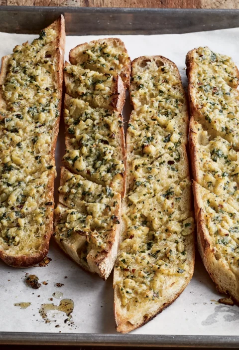 Ina Garten outrageous garlic bread on a parchment-lined sheet pan, with baguette pieces topped with golden Parmesan, garlic and parsley