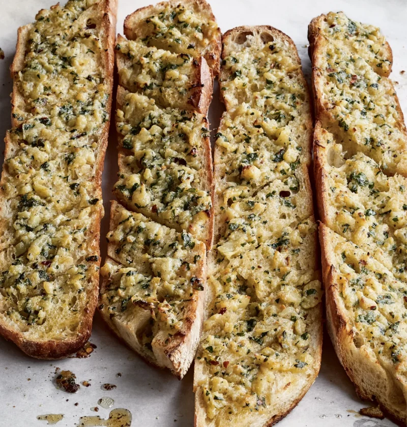 Ina Garten outrageous garlic bread on a parchment-lined sheet pan, with baguette pieces topped with golden Parmesan, garlic and parsley