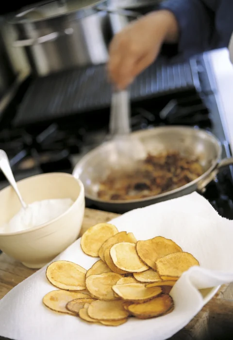 Ina Garten pan-fried onion dip in a cream bowl beside a skillet of caramelized onions and a plate of homemade potato chips