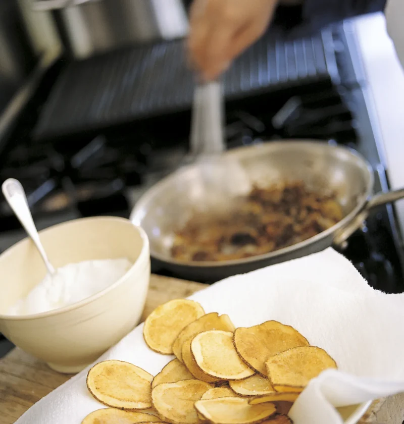 Ina Garten pan-fried onion dip in a cream bowl beside a skillet of caramelized onions and a plate of homemade potato chips