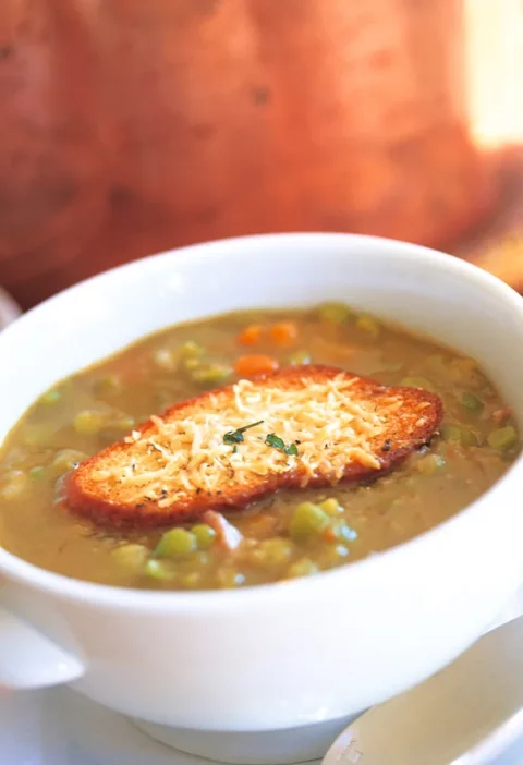 Ina Garten Parker's split pea soup in a white bowl topped with a Parmesan crouton, with carrots and peas visible