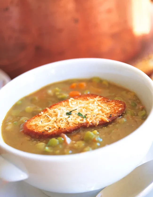 Ina Garten Parker's split pea soup in a white bowl topped with a Parmesan crouton, with carrots and peas visible