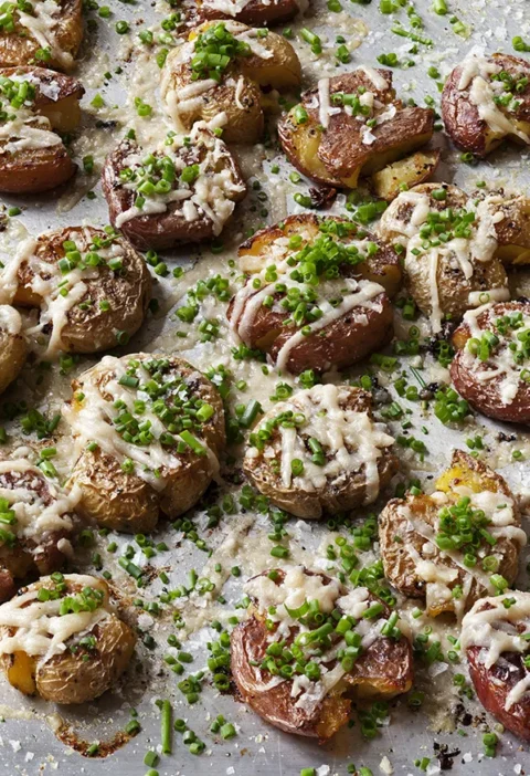 Ina Garten Parmesan chive smashed potatoes on a sheet pan topped with melted cheese and minced chives